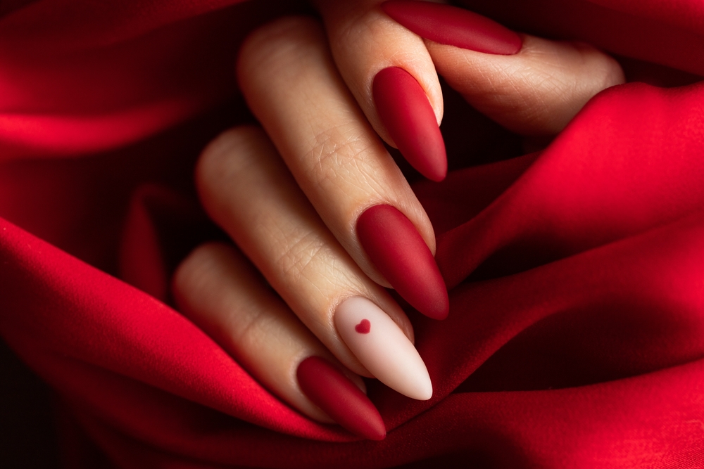 O femei cu unghii roșii, pozate pe un fundal dintr-un material roșu