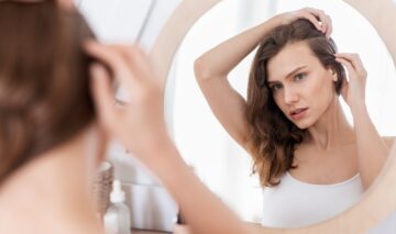 O femeie frumoasă care se privește în oglindă pentru a vedea dacă are nevoie de un tratament de exfoliere a scalpului