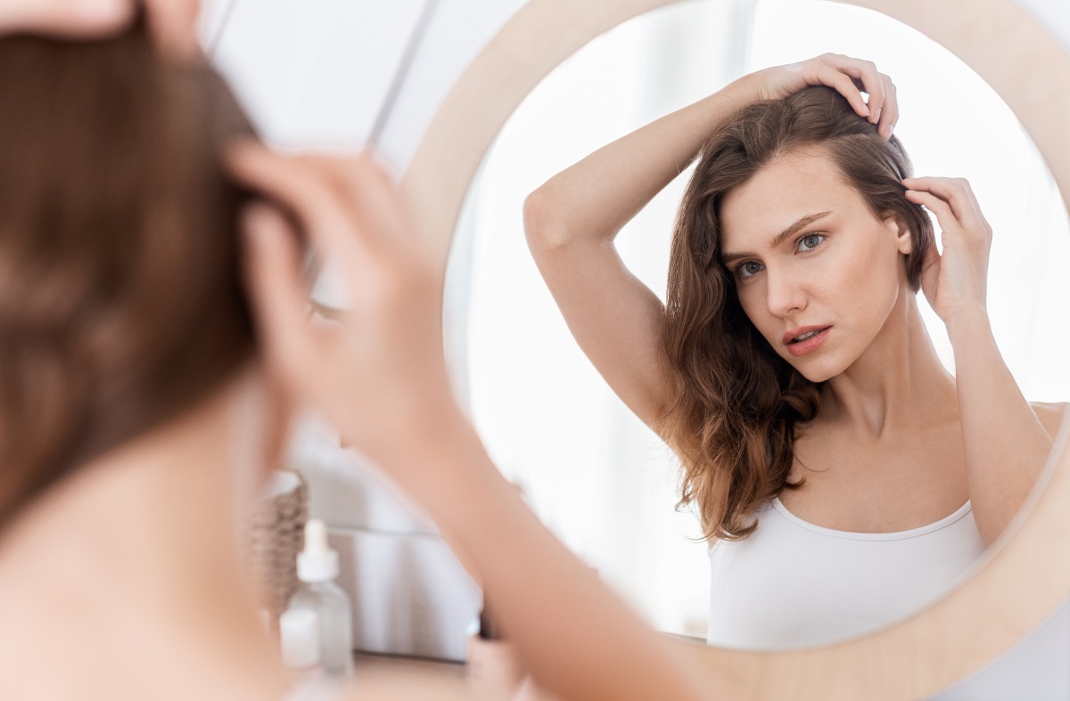 O femeie frumoasă care se privește în oglindă pentru a vedea dacă are nevoie de un tratament de exfoliere a scalpului