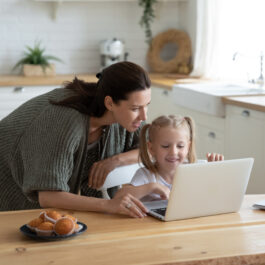 O mamă care stă cu fetița ei și privesc amândouă pe laptop