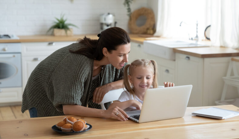 O mamă care stă cu fetița ei și privesc amândouă pe laptop