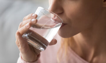O femeie care bea apă dintr-un pahar transparent