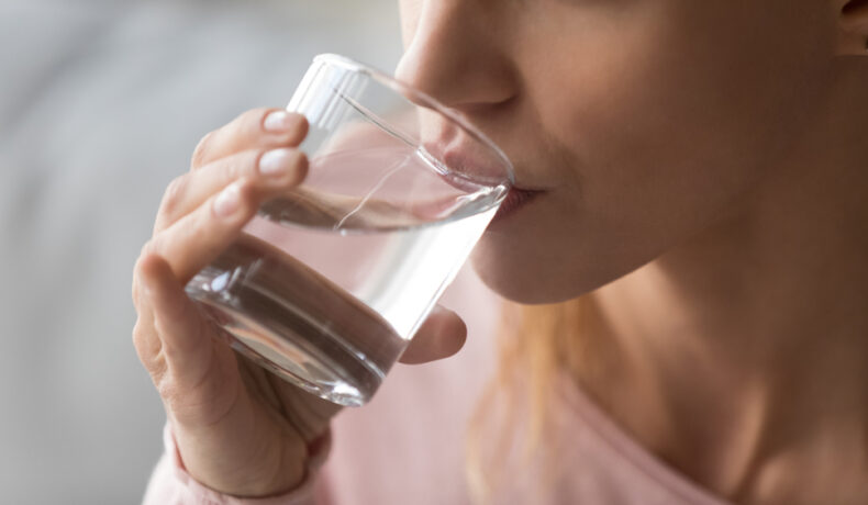O femeie care bea apă dintr-un pahar transparent