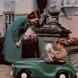 Regina Elisabeta în timp ce-l privește pe fiul său, Prințul Charles care se dă cu o mașinuță în anul 1952