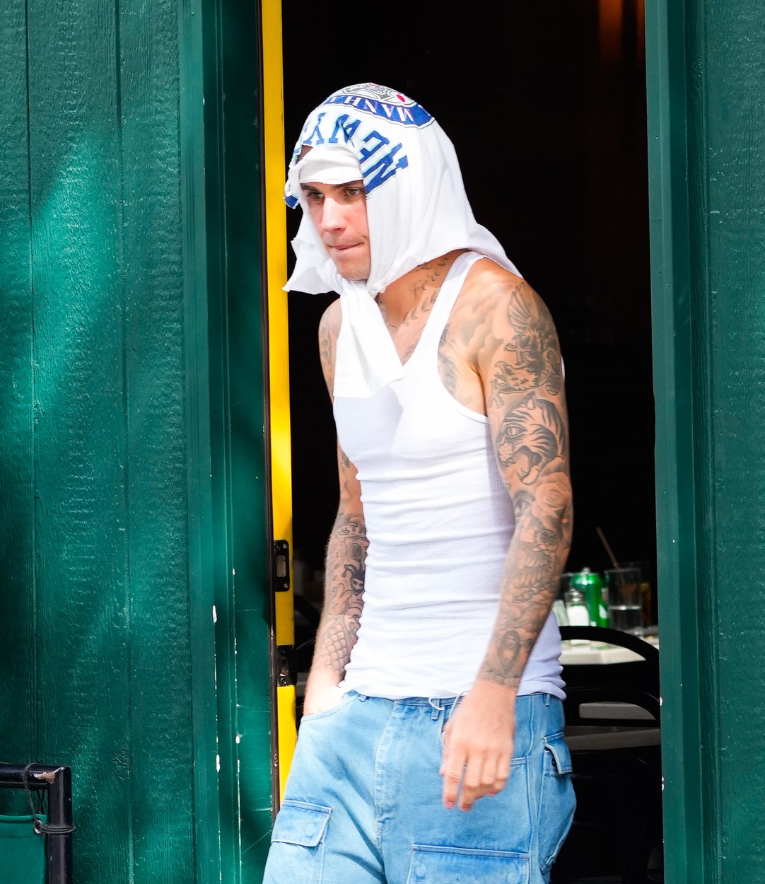 Justin Bieber, cu un tricou alb pe cap, într-un maiou alb și blugi largi