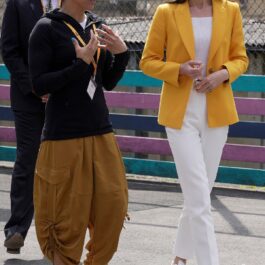Kate Middleton într-un sacou galbenși o pereche de pantaloni labi în timp ce discută cu o profesoară de sport