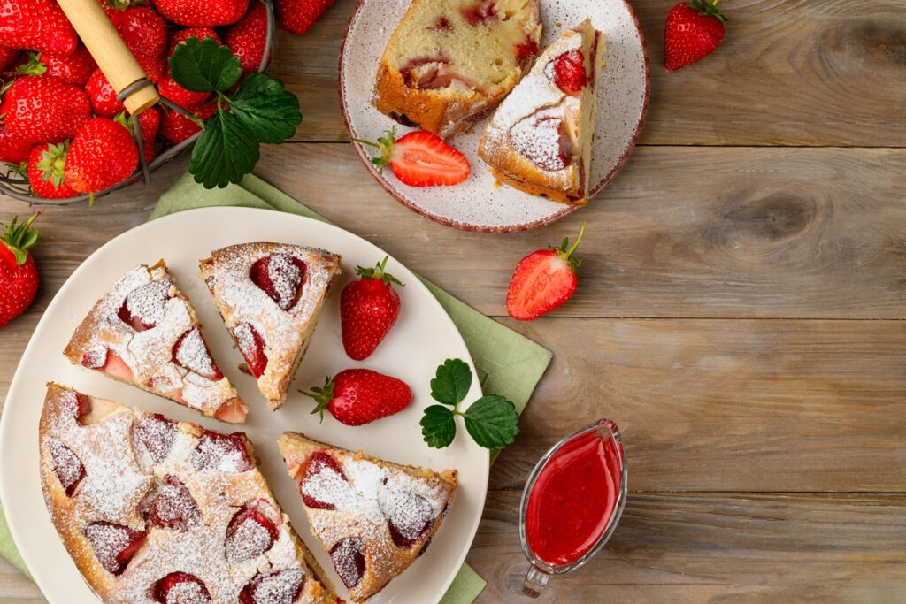 Prăjitură rotundă cu căpșuni, porționată pe platou și pe farfurie, alături de căpșuni proaspete