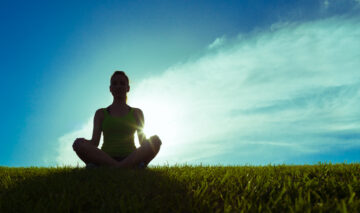 Fată care meditează pe un fundal albastru direct în soare pe o pajiște