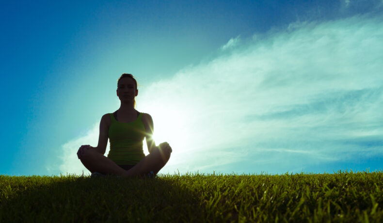 Fată care meditează pe un fundal albastru direct în soare pe o pajiște
