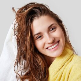 O femeie frumoasă cu părul umed care se șterge cu un prosop alb pentru a ilustra cum să-ți speli părul fără șampon
