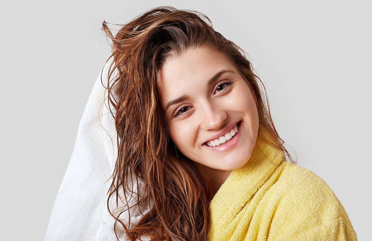 O femeie frumoasă cu părul umed care se șterge cu un prosop alb pentru a ilustra cum să-ți speli părul fără șampon