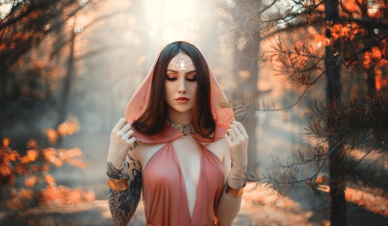 Fată frumoasă îmbrăcată într-o rochie lungă de voal stă într-o pădure
