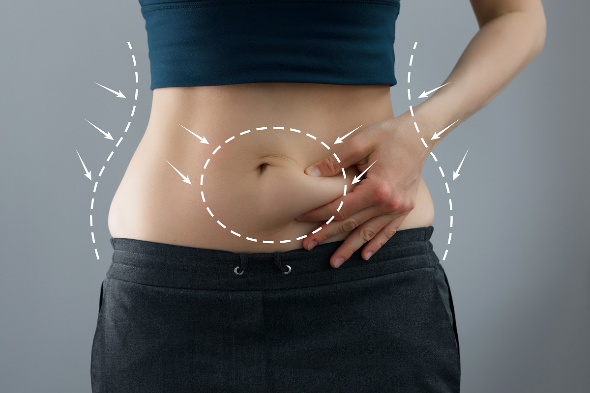 O femeie care își ciupește abdomenul pentru a ilustra câteva trucuri pentru a reduce grăsimea abdominală