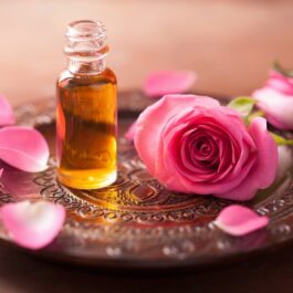 O tavă pe care se află ulei esențial din petale de trandafiri alături de un trandafir roz