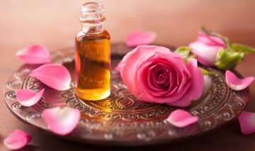 O tavă pe care se află ulei esențial din petale de trandafiri alături de un trandafir roz