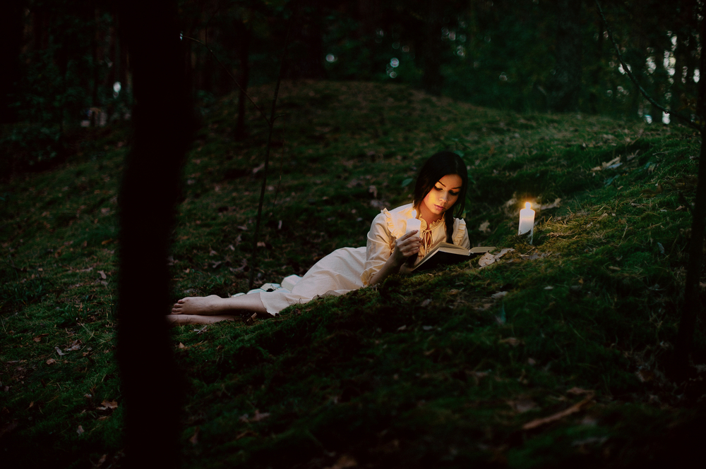 O femeie care stă la lumina lumânării și citește dintr-o carte