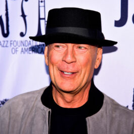 Bruce Willis, îmbrăcat în culori închise, cu o pălărie neagră pe cap, la un eveniment