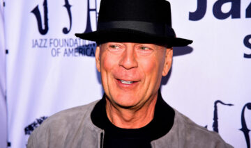 Bruce Willis, îmbrăcat în culori închise, cu o pălărie neagră pe cap, la un eveniment