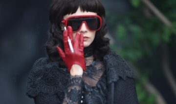 Cara Delevingne, cu ochelari de soare cu rame roșii, într-o ținută de culoare neagră