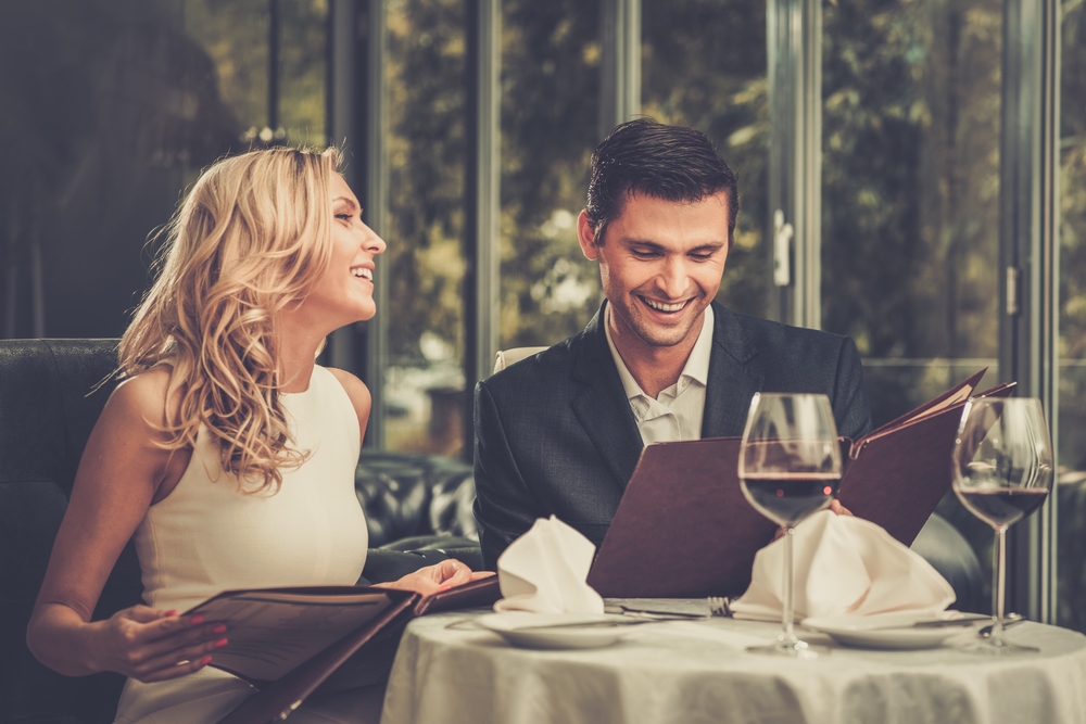 Fată frumoasă care zâmbește alături de un bărbat la restaurant se uită în meniuri