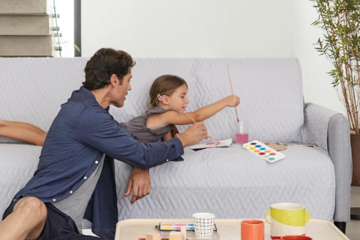 Un tată care o ajută pe fiica lui să picteze pe o canapea cu husă