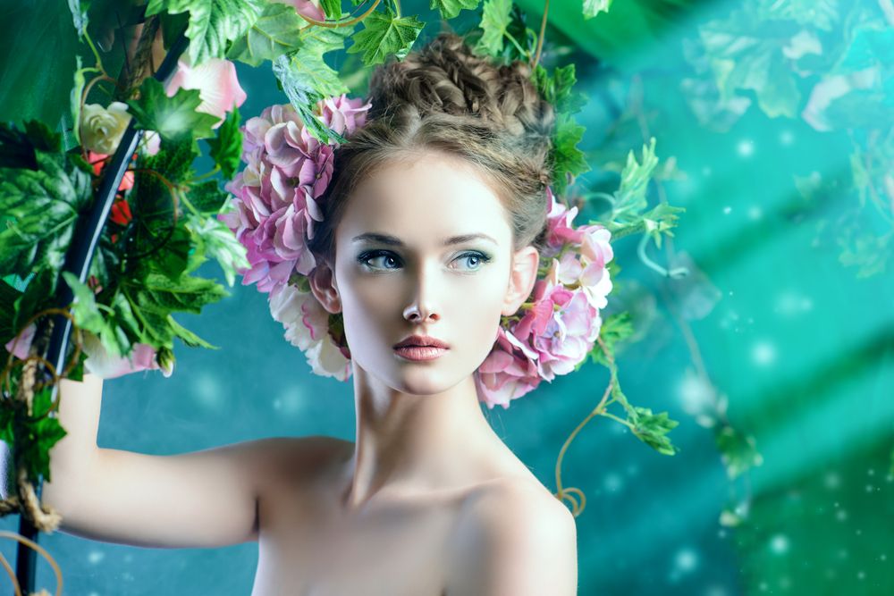 O femeie tânără cu flori prinse în păr care stă sub o iederă înflorită