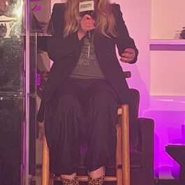 Christina Applegate, pe un scaun, îmbrăcată în negru, fotografiată în timp ce vorbește la un microfon