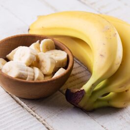 Trei banane alături de un bol plin cu felii de banane pentru a ilustra beneficiile acestora