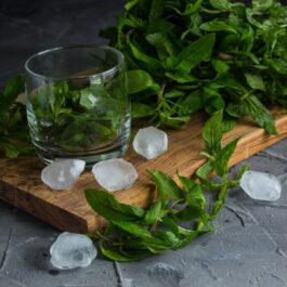 Frunze de mentă, un pahar și cuburi de gheață pe un tocător