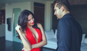 O femeie într-o rochie roșie, decoltată, în timp ce flirtează cu un bărbat