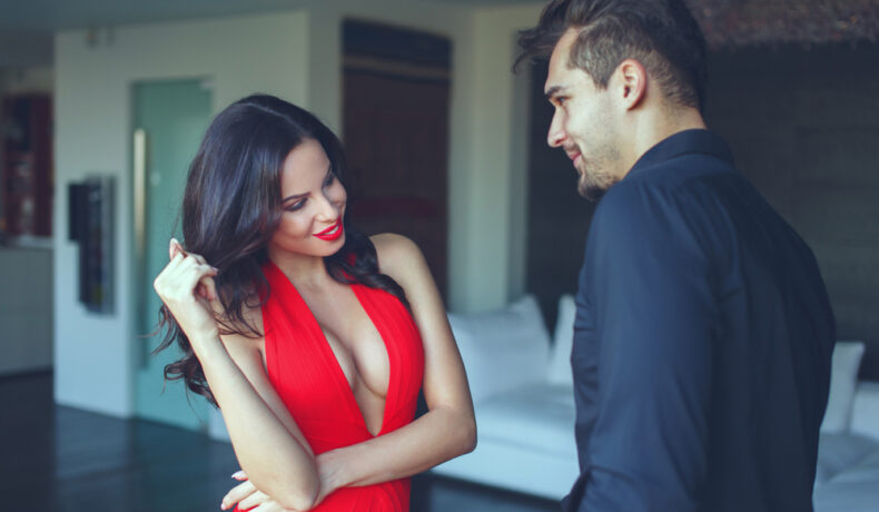 O femeie într-o rochie roșie, decoltată, în timp ce flirtează cu un bărbat