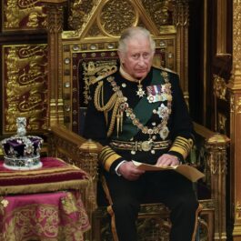 Regele Charles în timp ce stă pe tron alături de coroana purtată de Regina Elisabeta în ziua încoronării sale