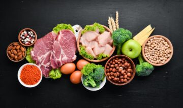 Omasă neagră pe care se află alimente bogate în proteine cum ar fi carnea, lintea, broccoli, mere, pentru a ilustra câteav semne care indică un consum prea mare de proteine