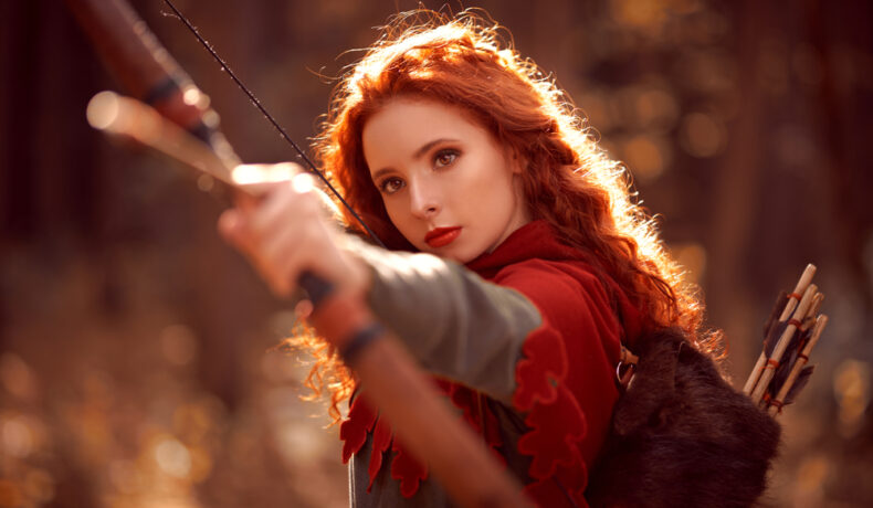 Fată frumoasă cu părul roșcat ține un arc cu săgeți în mână