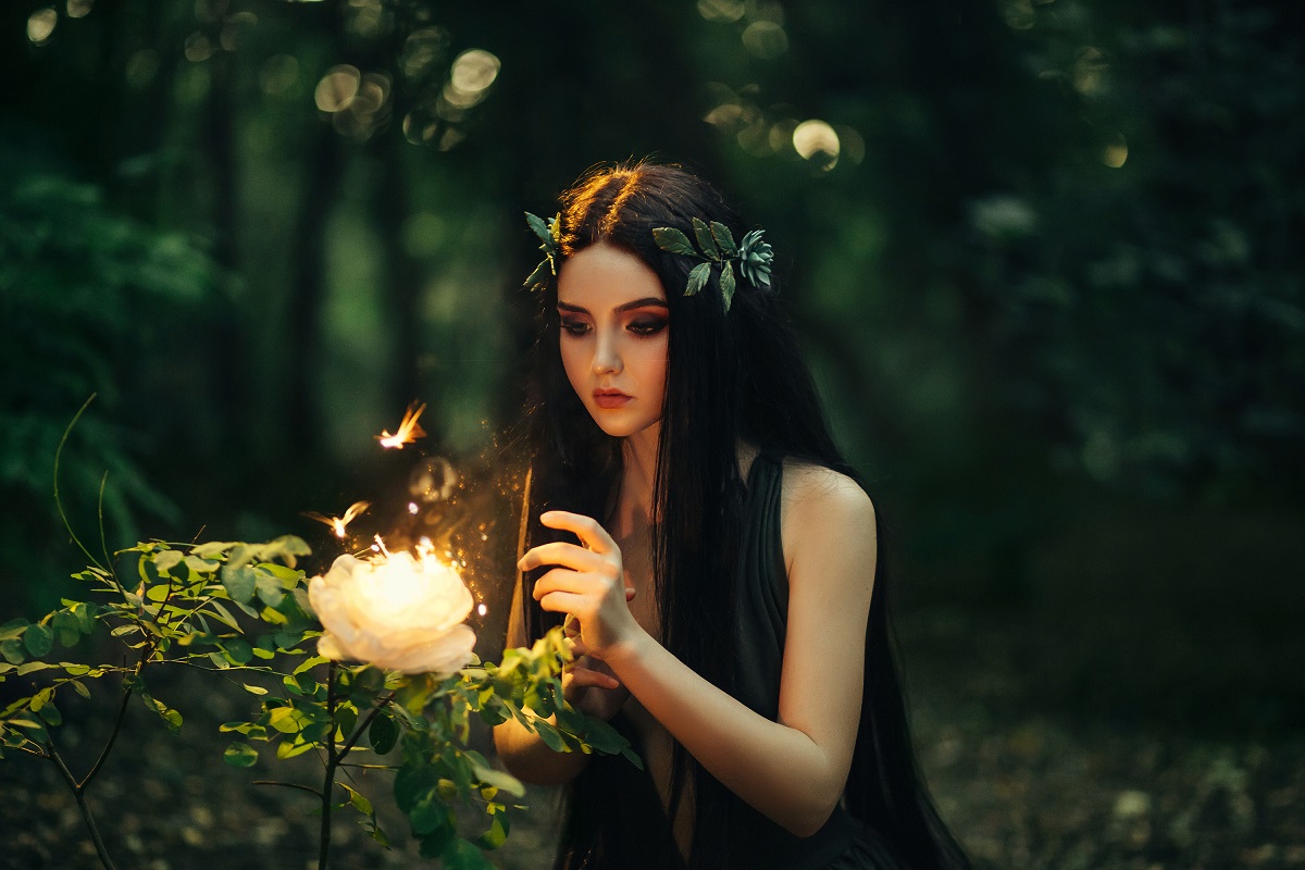 O femeie frumoasă care privește o floare dintr-o pădure pentru a ilustra una dintre zodiile a căror inimă s-a întărit în 2023