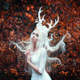 Fată frumoasă cu părul alb, îmbrăcată într-o rochie albă stă într-o pădure