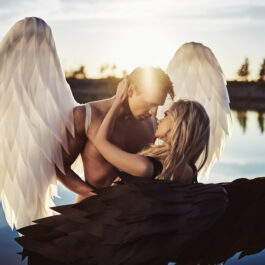 Un cuplu cu aripi de îngeri care stau pe malul unui lac îmbrățișați