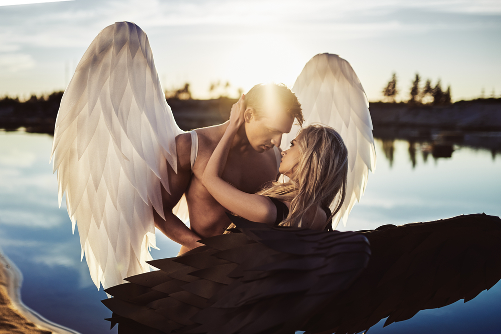 Un cuplu cu aripi de îngeri care stau pe malul unui lac îmbrățișați