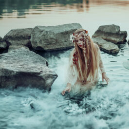 O tânără este înconjurată de crini și stânci, în apele unui lac
