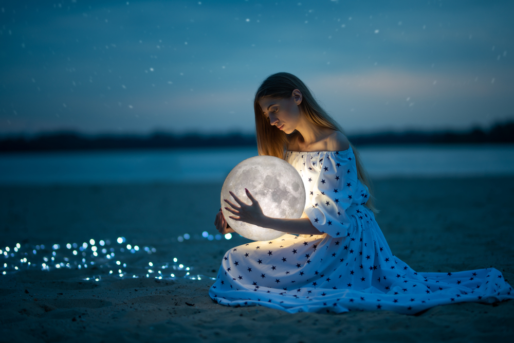 O femeie în rochie albă cu buline, care ține o lună luminoasă în mână