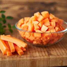 Mai mulți morcovi tăiați într-un castron, pe un blat de bucătărie din lemn