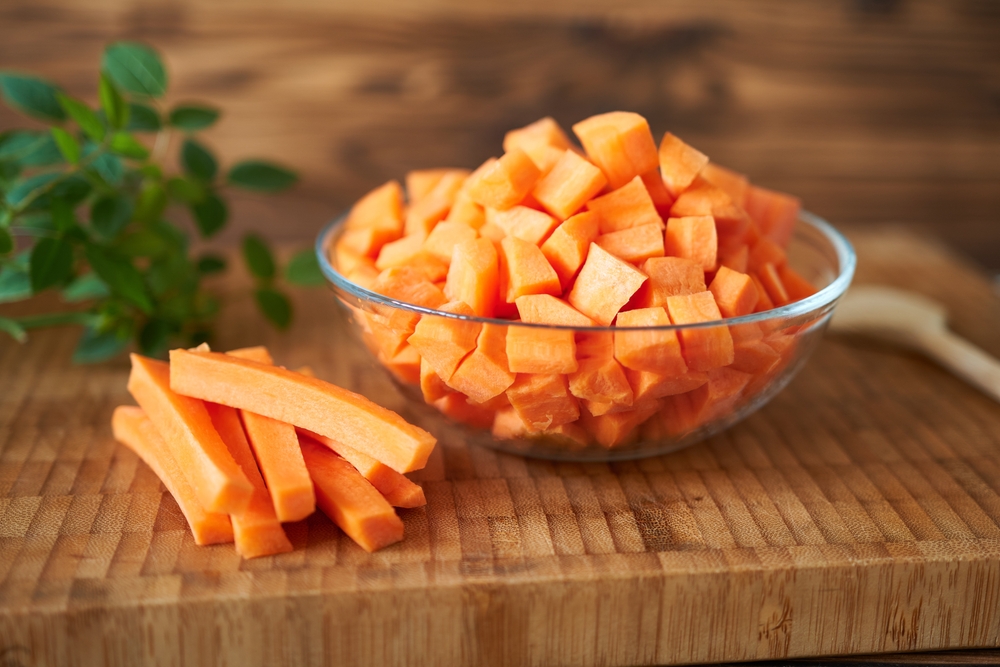 Mai mulți morcovi tăiați într-un castron, pe un blat de bucătărie din lemn