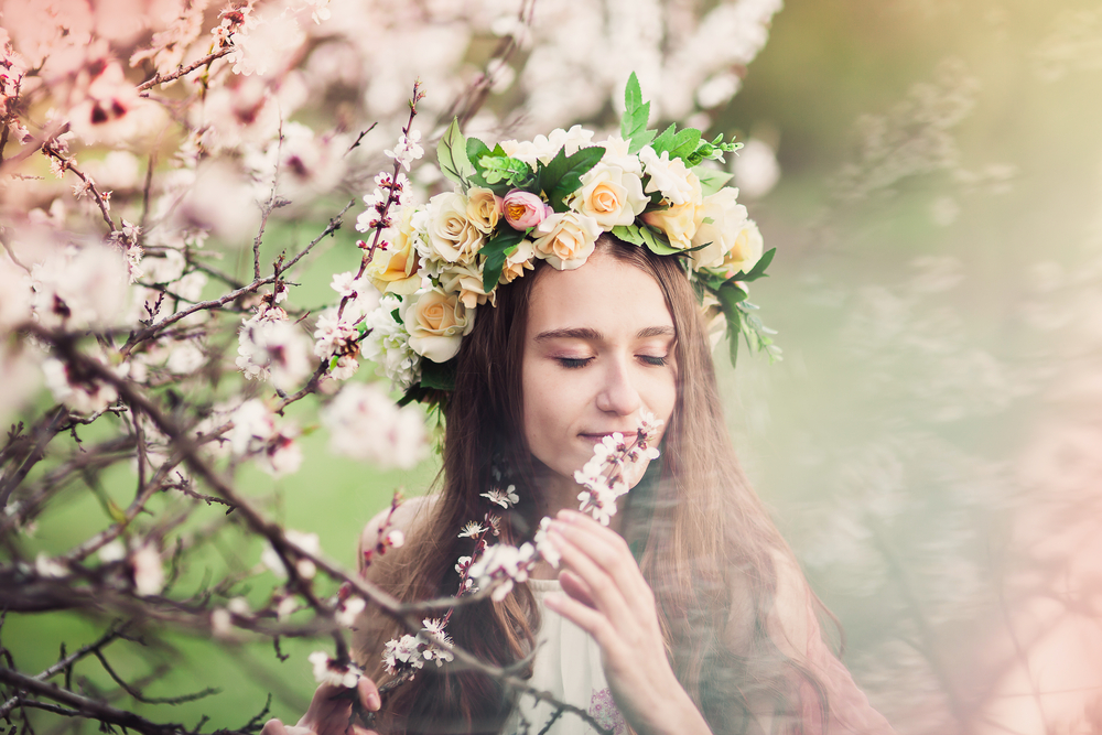 Fată frumoasă cu părul lung cu o coroniță de flori pe cap stă într-o poieniță cu copaci înfloriți