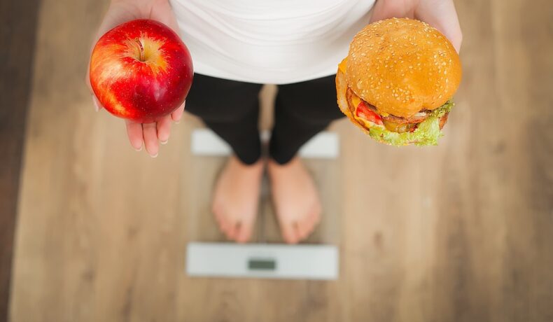 O femeie care ține în mână un măr și un burger pentru a ilustra câte kilograme e recomandat să ai după vârsta de 40 de ani