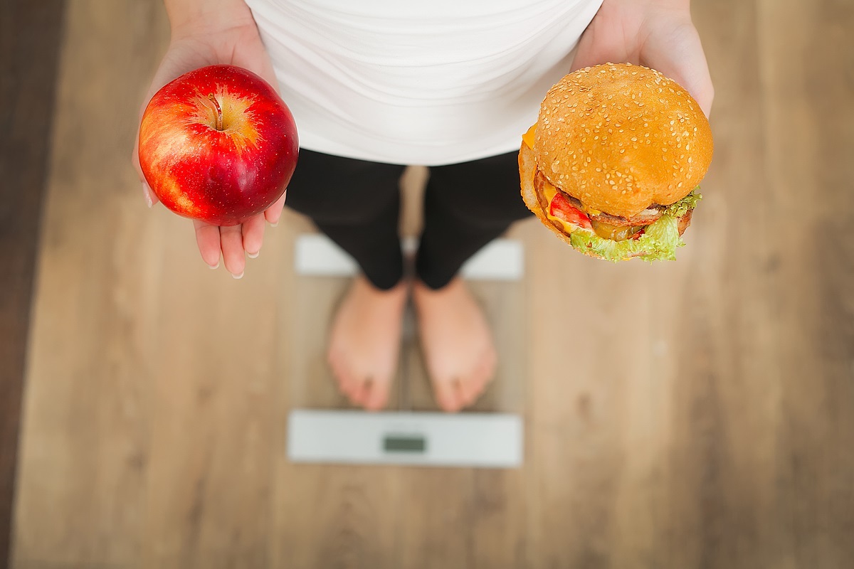 O femeie care ține în mână un măr și un burger pentru a ilustra câte kilograme e recomandat să ai după vârsta de 40 de ani