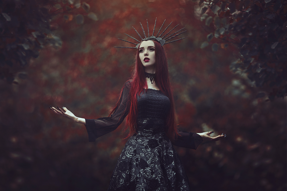 Fată frumoasă îmbrăcată într-o rochie lungă, neagră stă într-o pădure întunecată