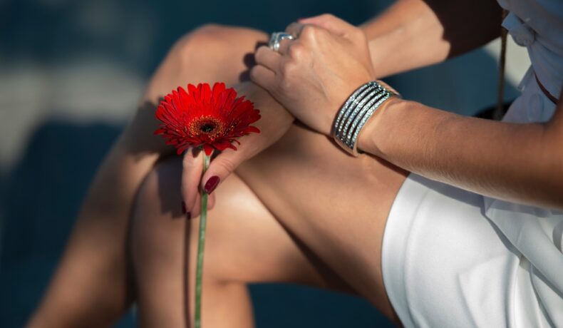 O femeie care stă picior peste picior și are o floare roșie în mână