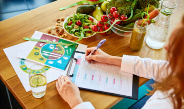 O femeie care are mai multe ingrediente sănătose pe masă și ține un jurnal de dietă