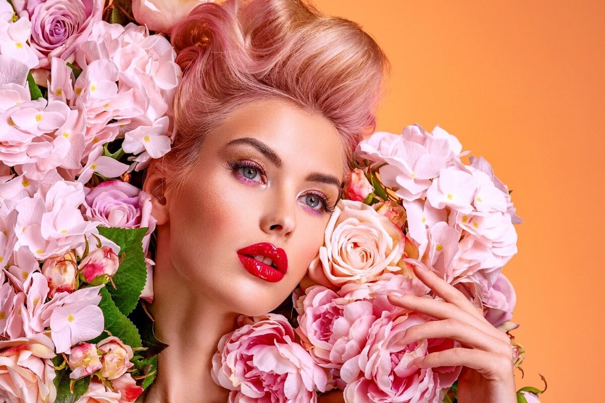 O femeie frumoasă cu o nunță de blond la păr care stă printre trandafiri roz