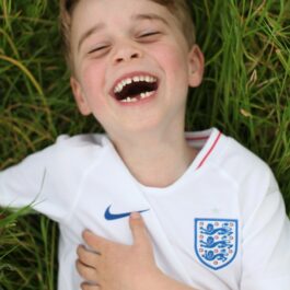 Prințul George în timp ce stă întins pe iarbă și râde